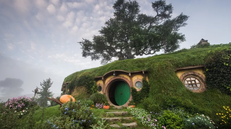 Hobbit house built into a green hillside with round door and lush garden at Hobbiton Movie Set in Matamata New Zealand.