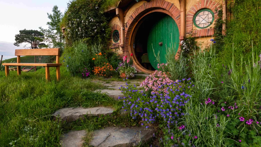 A round green door set into a hillside with flowering plants and a stone path at the Hobbiton Movie Set
