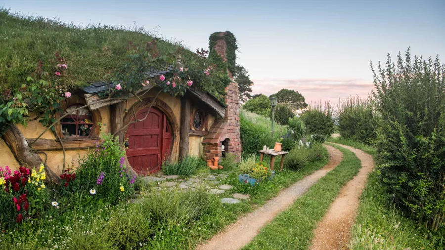 Traditional hobbit house with a red door beside a winding dirt path at the Hobbiton Movie Set near Matamata