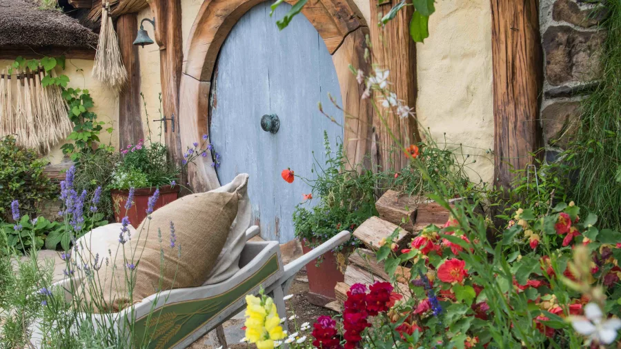 A blue round-door Hobbit hole nestled among lush flowers and greenery at Hobbiton Movie Set