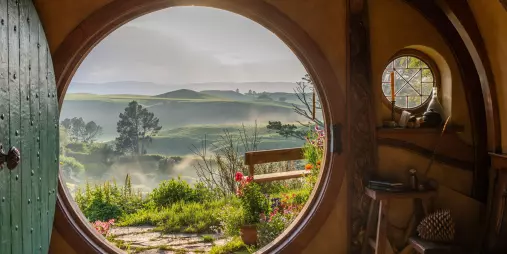Iconic round doorway view from inside Bag End, looking out to misty hills and garden paths in Hobbiton, New Zealand