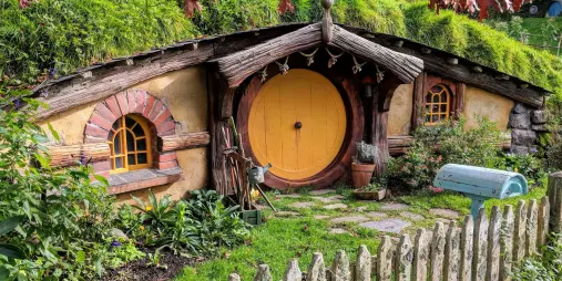Hobbit house with a yellow round door, rustic garden, and wooden picket fence at the Hobbiton Movie Set