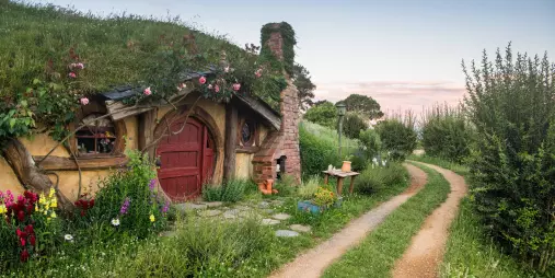 Traditional hobbit house with a red door beside a winding dirt path at the Hobbiton Movie Set near Matamata