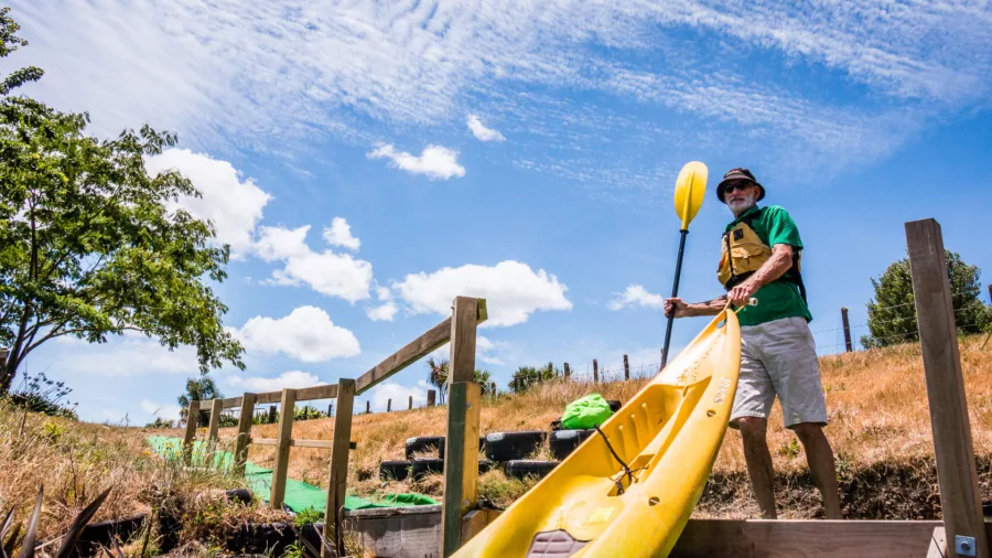 Man carrying a yellow kayak to the Waikato River launch point on a sunny summer day