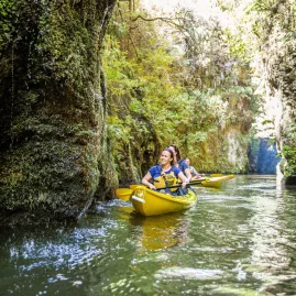 Group of kayakers smiling while exploring narrow cliffs and lush greenery on Lake Karapiro near Cambridge