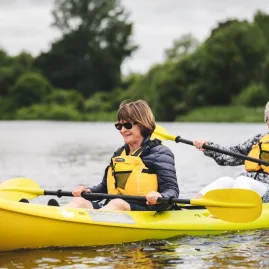 Two senior women kayaking on Lake Karapiro in Waikato, smiling and enjoying the calm waters
