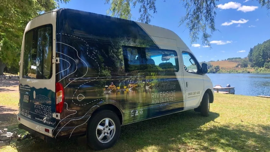 Riverside Adventures shuttle van parked beside a scenic lake in Waikato