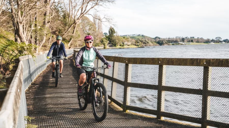 Two cyclists riding along a boardwalk section of the Te Awa River Ride beside the water