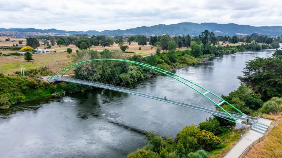 Aerial view of a cyclist crossing a green arch bridge over the Waikato River
