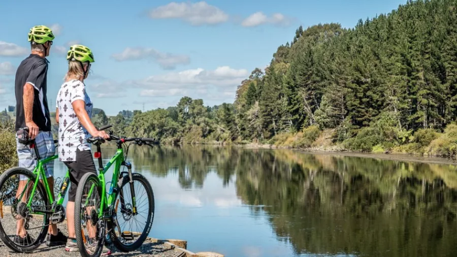 Couple on bikes looking over a calm river with lush forest on the opposite bank