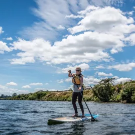 Woman paddleboarding on Waikato River under a bright blue sky