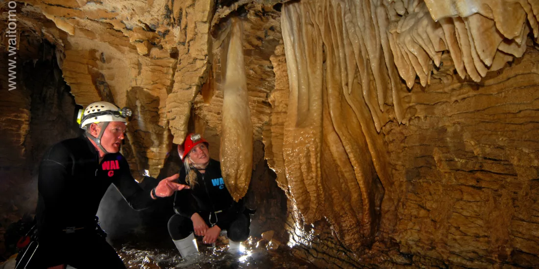 Two adventurers kneel beside dramatic limestone formations on the Haggas Honking Holes tour in Waitomo