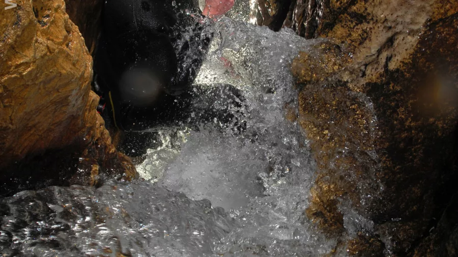 Caver descending a narrow limestone crevice with water rushing past in Haggas Honking Holes, Waitomo