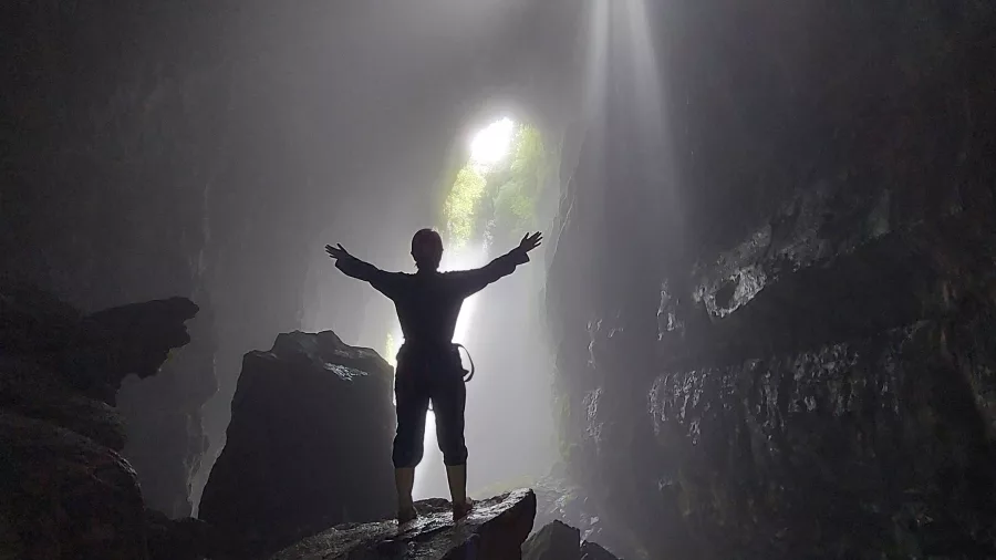 Caver silhouetted under light shafts in a Waitomo cave