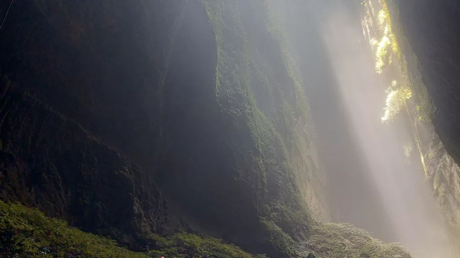 Explorers hiking in sinkhole with sunbeam in Waitomo