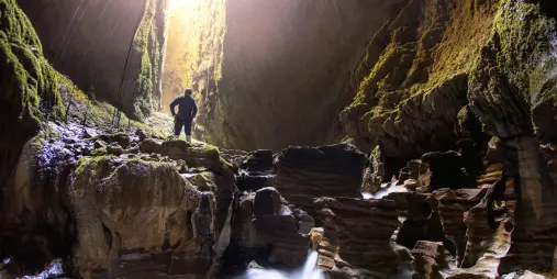 Explorer standing above flowing water inside the Lost World cave in Waitomo surrounded by limestone formations