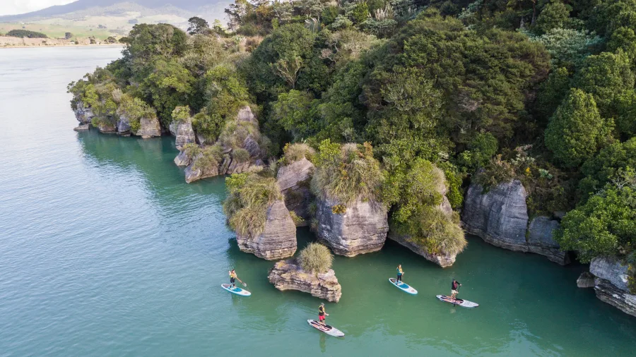 Paddleboarders exploring the limestone cliffs along Raglan’s coast in Waikato.