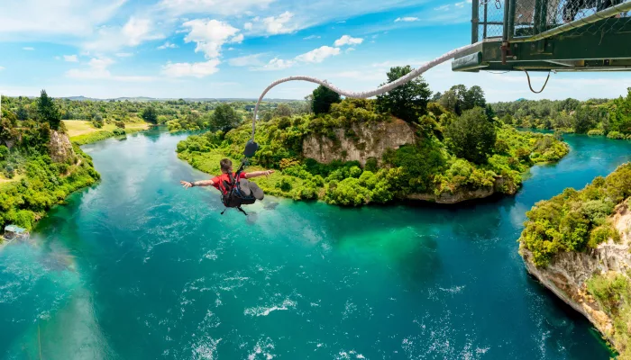 Man jumping from Taupō Bungy platform over the turquoise waters of the Waikato River in New Zealand.