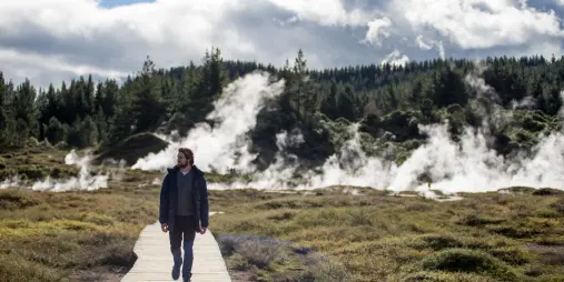 Man walking along a boardwalk with steam vents in the background at Craters of the Moon in Taupo, New Zealand.