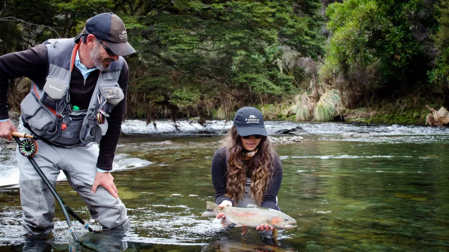 Woman holding a rainbow trout in a clear river while fly fishing with a guide in Taupo, New Zealand.