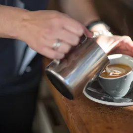Barista pouring steamed milk into a freshly brewed coffee at The Storehouse café in Taupō, New Zealand.