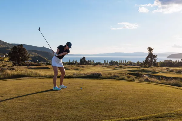 Golfer swinging on the Kinloch Golf Club championship course with Lake Taupō in the background.