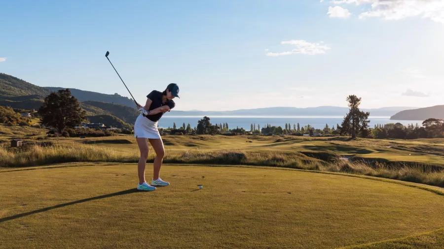 Golfer swinging on the Kinloch Golf Club championship course with Lake Taupō in the background.