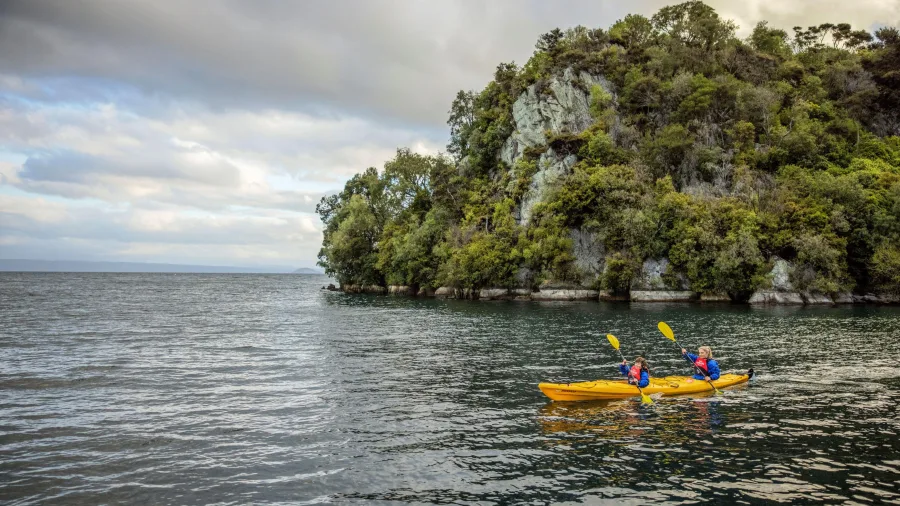 Two people kayaking near bush-clad cliffs on Lake Taupō