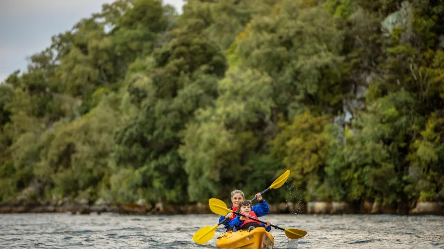 Mother and child kayaking together on Lake Taupō with native bush behind