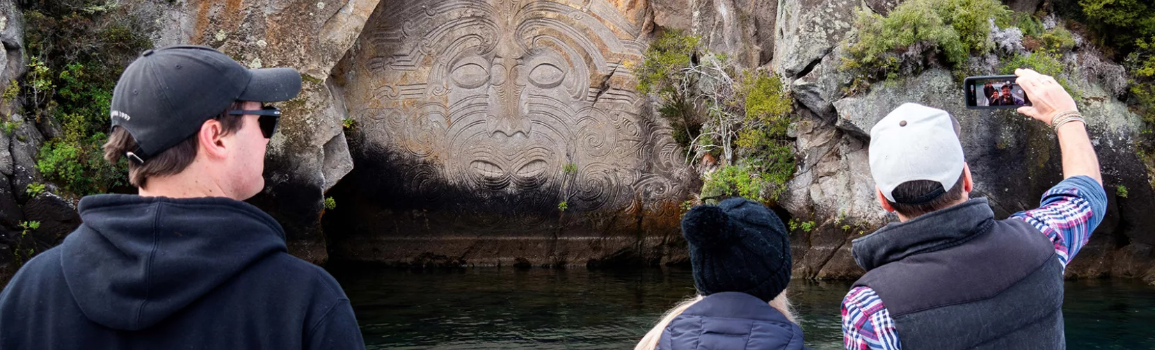 Tourists taking photos of the Ngatoroirangi Mine Bay Maori Rock Carvings from a boat on Lake Taupō