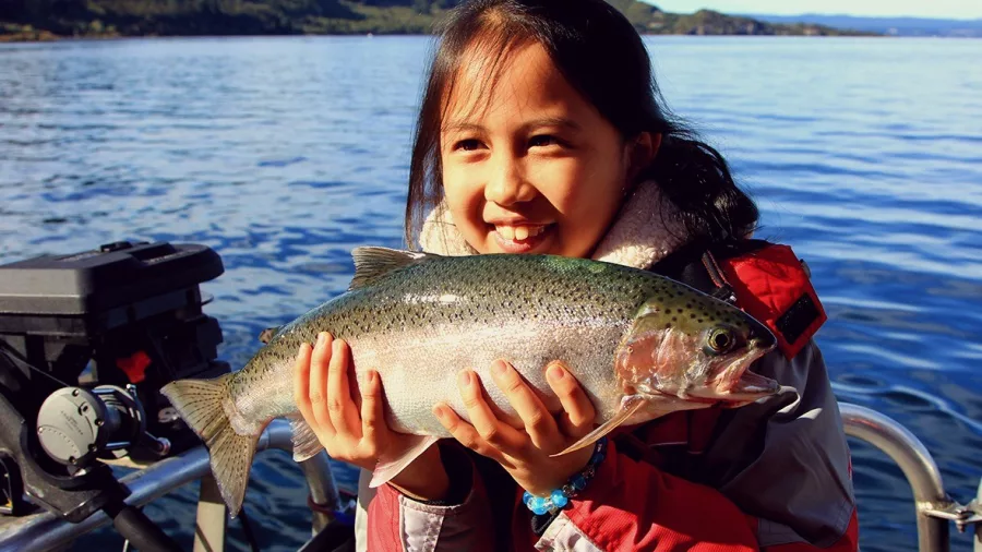 Smiling young girl proudly holding a freshly caught trout on Lake Taupō