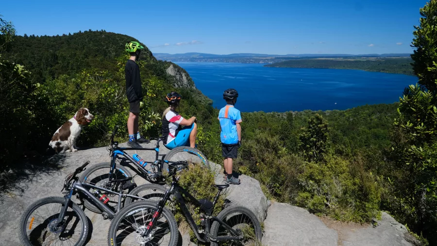 Children and a dog looking out over Lake Taupō with bikes resting nearby on the Great Lake Trail.