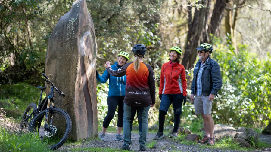 Guide explaining Māori history beside a carved stone along the river trail