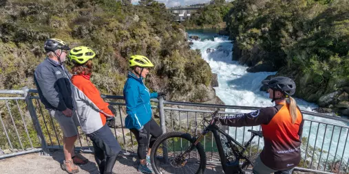 Group of cyclists stopping at a lookout point over Huka Falls while riding a scenic trail in Taupō, New Zealand.