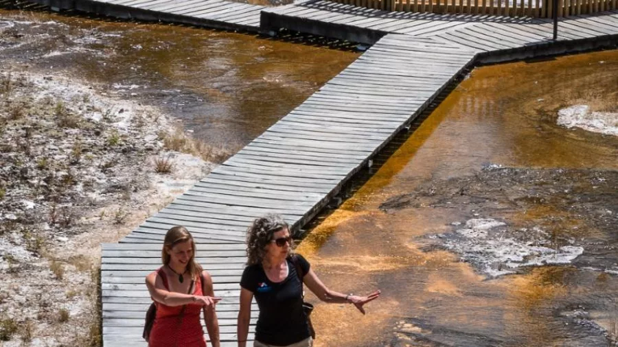Visitors walking along a geothermal boardwalk over orange silica terraces at Orakei Korako
