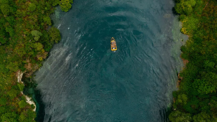 Aerial view of a yellow jet boat from Rapids Jet cruising along a calm section of the Waikato River near Taupō, surrounded by forest.