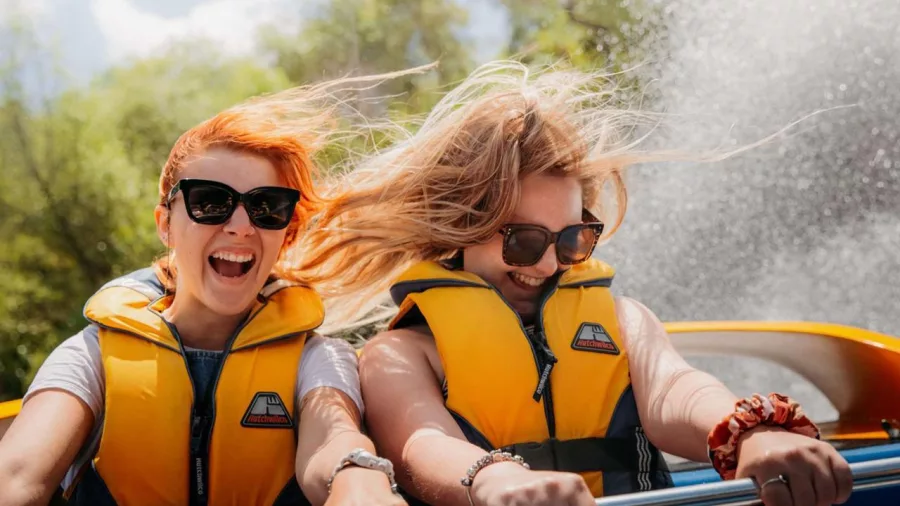 Two women enjoying the thrill of a Rapids Jet ride near Taupō, with water spraying and hair blowing in the wind.