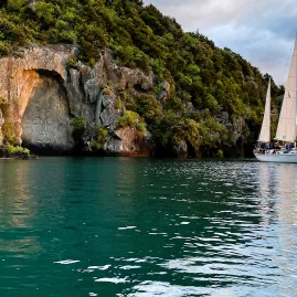 Sail Barbary cruising past the Māori Rock Carvings at Mine Bay during evening golden hour