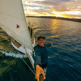 Man taking a selfie on the bow of Sail Barbary during a sunset cruise on Lake Taupō