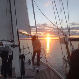 People standing on the deck of Sail Barbary, watching the sun set over Lake Taupō