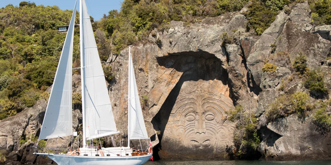 Sail Barbary yacht floating beside the Māori Rock Carvings in Taupō’s Mine Bay
