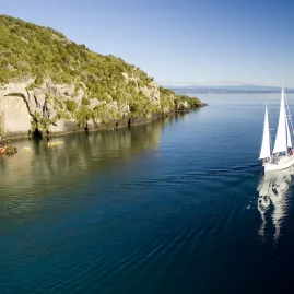 Sail Barbary yacht sailing toward Māori Carvings with kayaks nearby on Lake Taupō