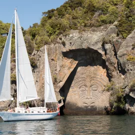 Sail Barbary yacht floating beside the Māori Rock Carvings in Taupō’s Mine Bay