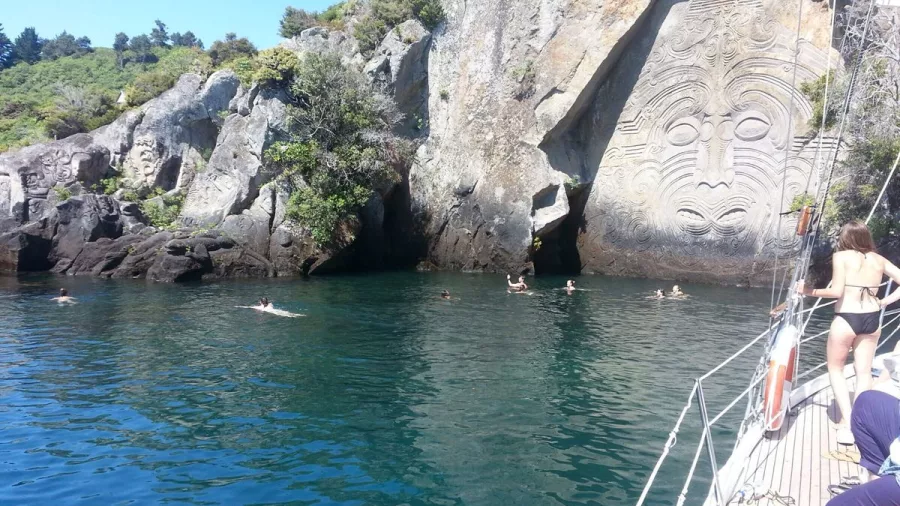 Swimmers enjoying the water in front of the Māori Rock Carvings at Mine Bay with Sail Barbary
