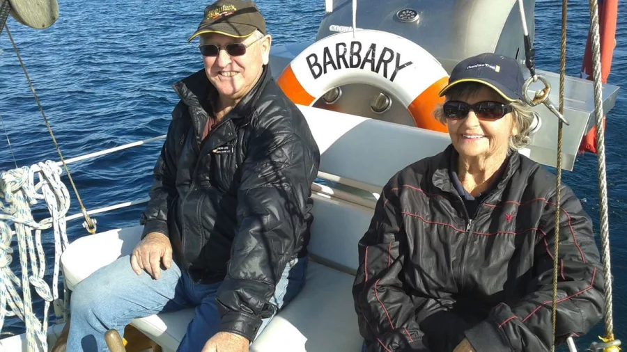 Older couple smiling while seated on Sail Barbary with Lake Taupō in the background