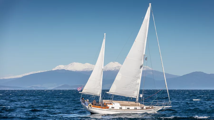 White sailboat on the deep blue waters of Lake Taupō with mountains behind