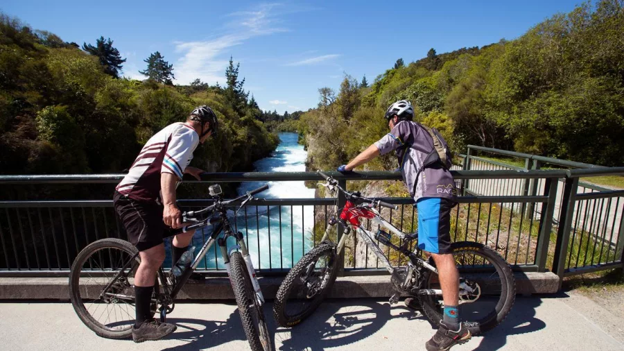 Two cyclists pausing on a bridge overlooking a fast-flowing river on the Rotary Ride trail in Taupō