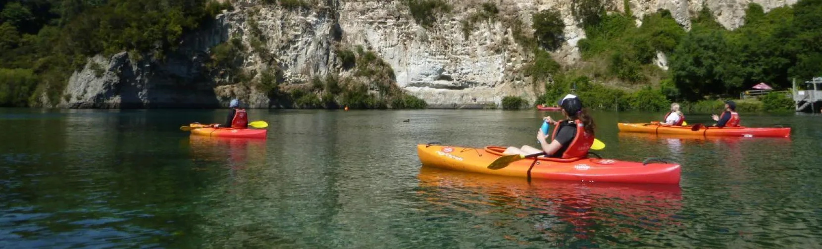 Group of kayakers paddling near white cliffs on the Waikato River in Taupō under clear blue skies
