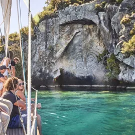 Passengers on a sailing boat viewing the Māori rock carvings at Mine Bay on Lake Taupō