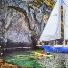Sailboat and kayakers near the Māori rock carvings at Mine Bay on Lake Taupō